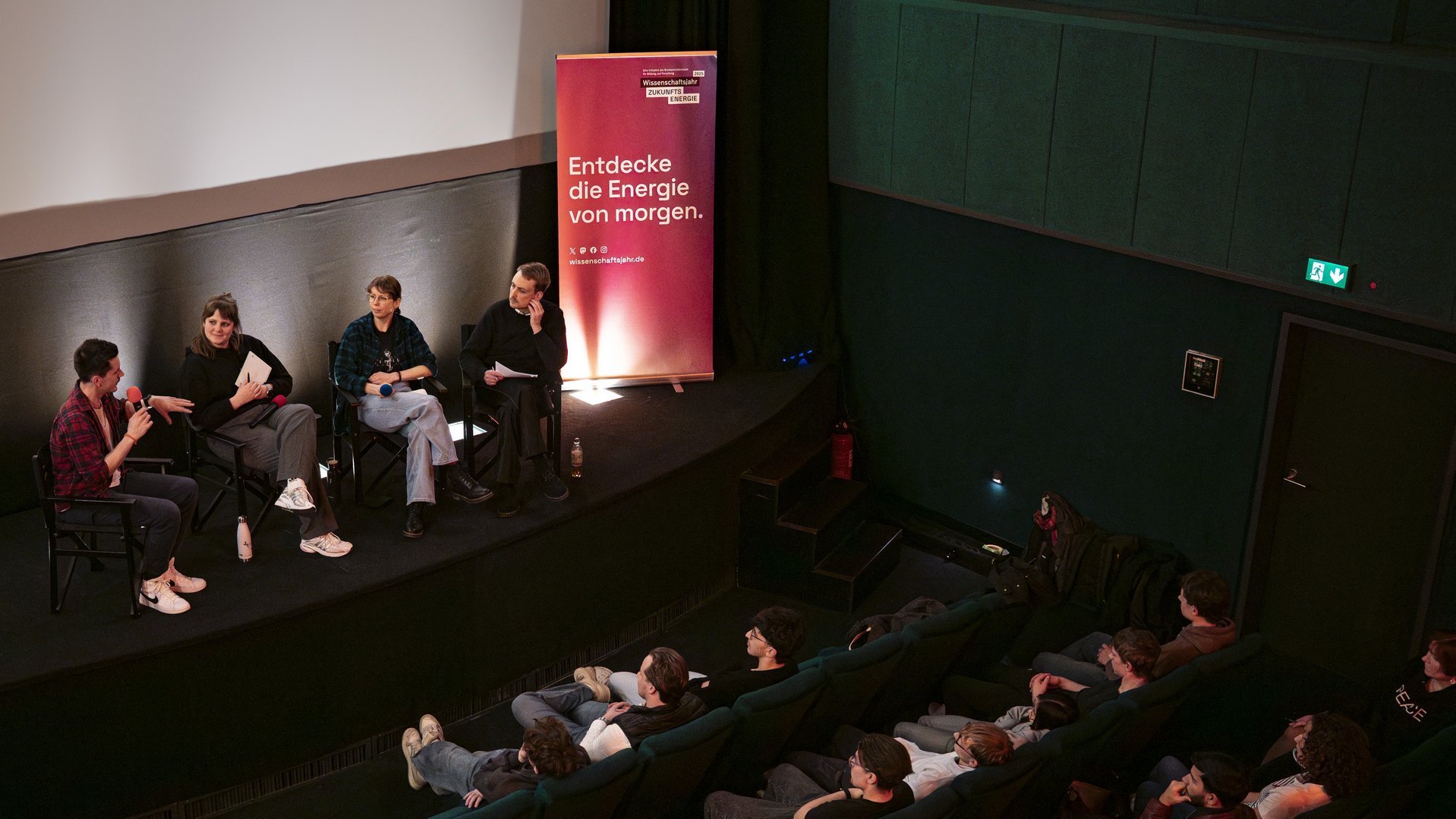 Vier Personen diskutieren in einem Kinosaal vor einer Schulklasse.