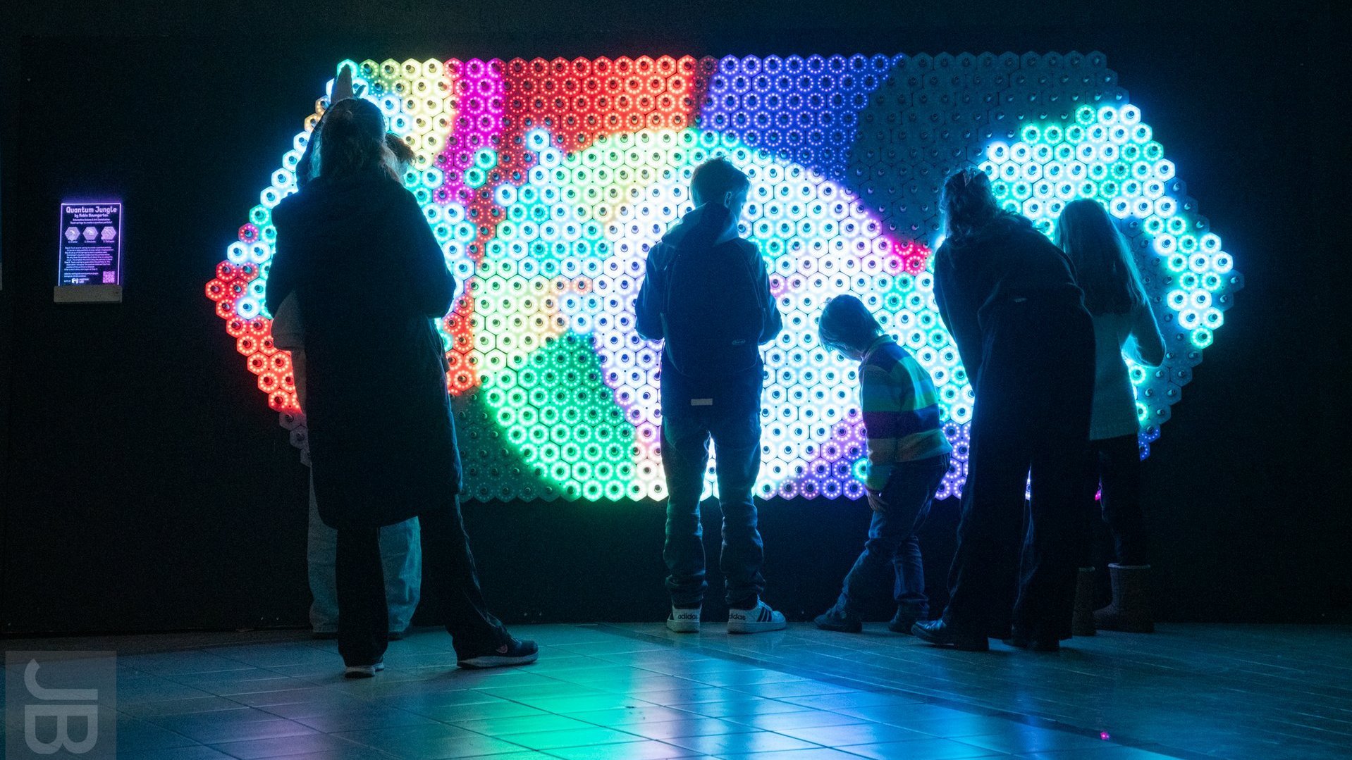 Junge Menschen stehen vor einer Wand aus bunten Lichtern.