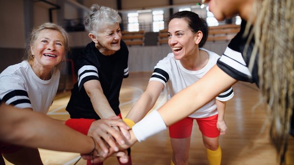 WJ26_Frauengesundheit_Altersgruppen Eine Sportmannschaft aus Frauen unterschiedlichen Alters hält die Hände in ihre Mitte.
