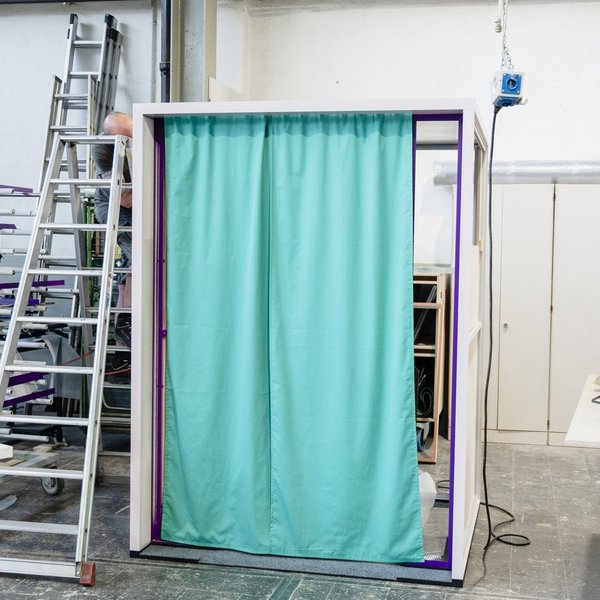 Außenansicht der Erzählbox während des Bauprozesses in der Werkstatt. Das Gerüst trägt einen grünen Vorhang.