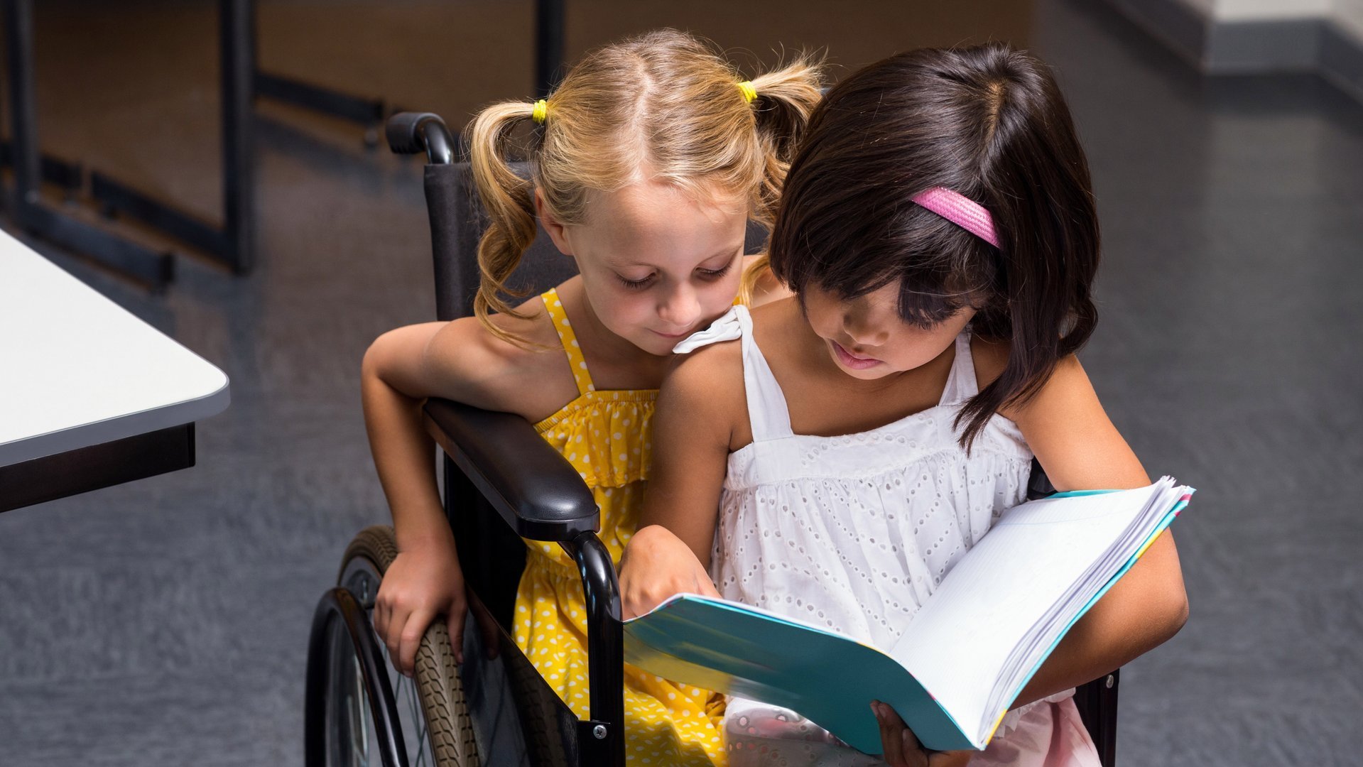 Zwei Kinder sitzen zusammen in einem Rollstuhl und lesen.